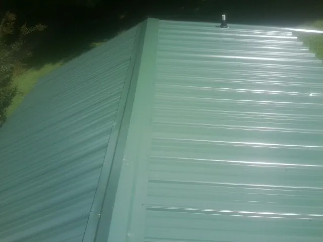 New green metal panels meeting at the ridge of a roof — Flat Roof Repair work by our crew in Harrisburg