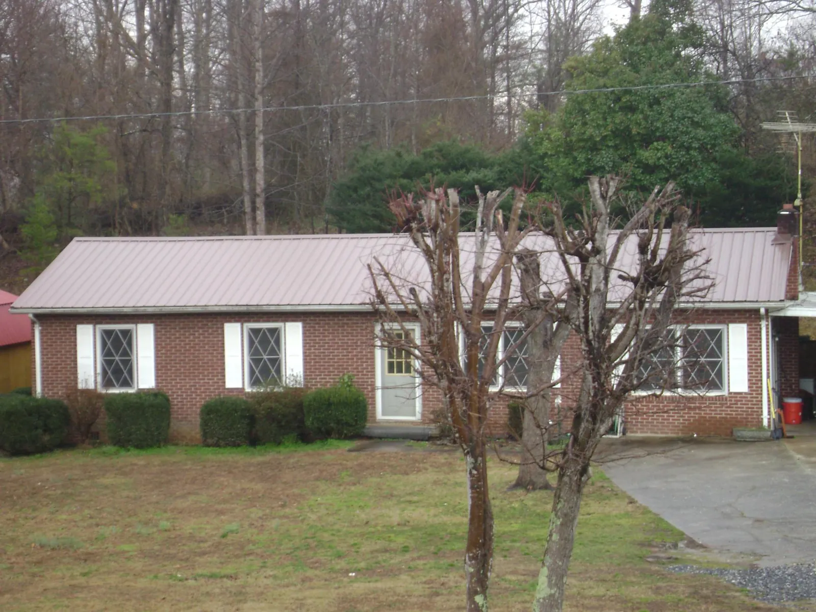 Mauve metal roof on a brick ranch home behind bare trees in Harrisburg